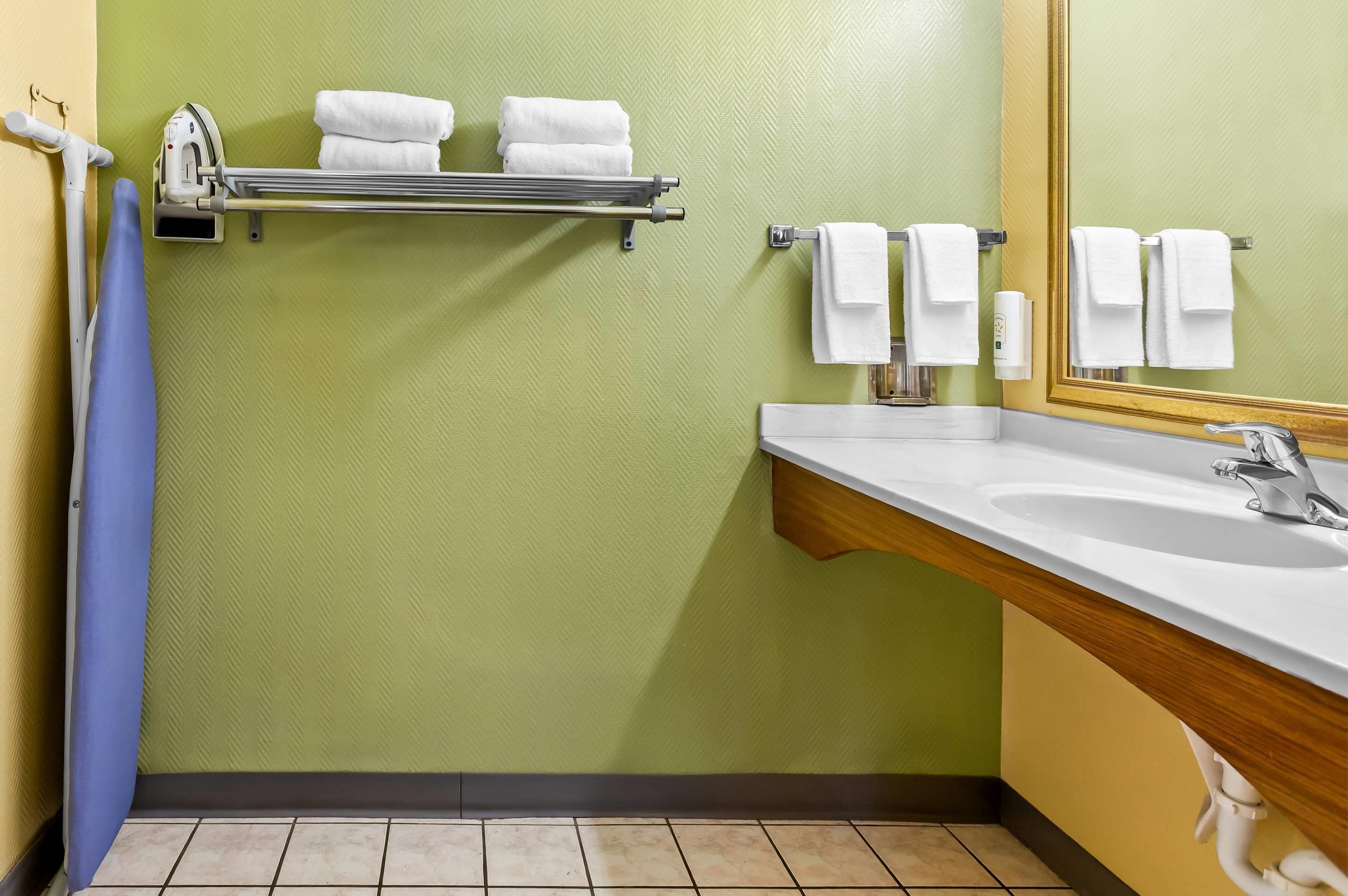 Une salle de bain avec un mur vert, un lavabo blanc et un miroir. Des serviettes sont suspendues à un porte-serviettes et il y a un rideau de douche bleu.