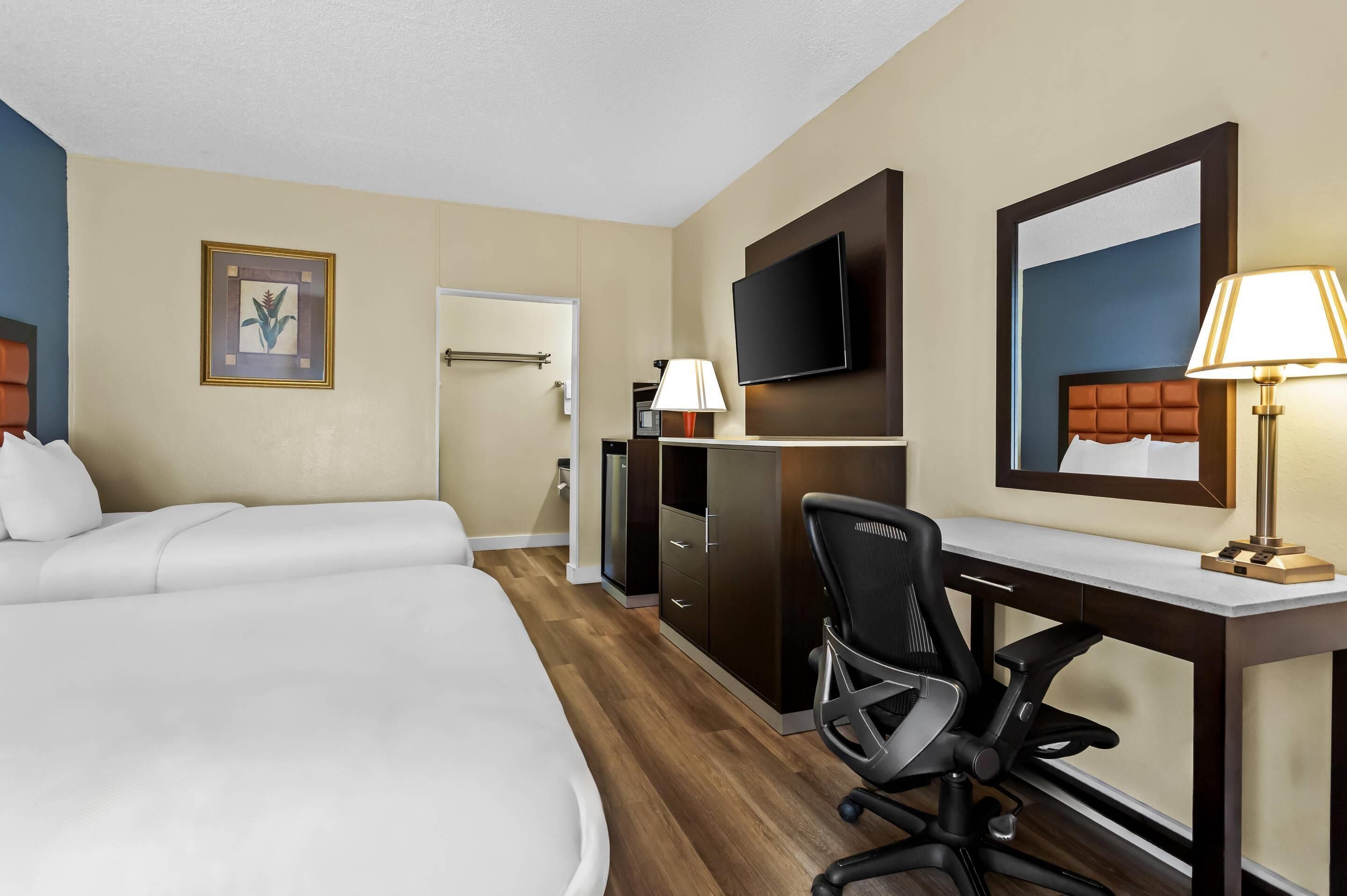 Una habitación de hotel con dos camas, un escritorio, una silla, un televisor y una lámpara.