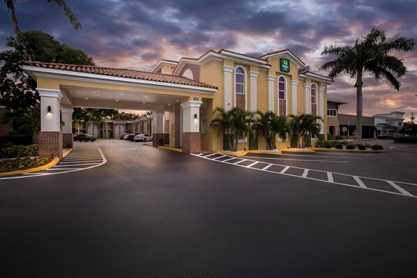 A hotel with a covered parking area, palm trees, and a sunset sky. - Quality Inn Tampa Airport - Cruise Port (Tampa)