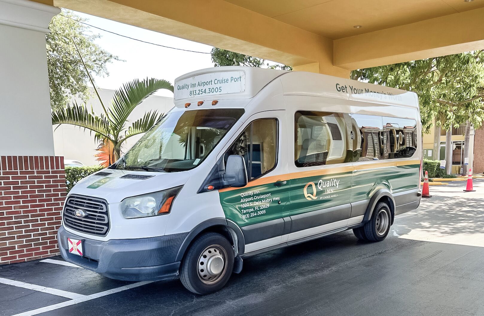 A white and green bus with "Quality Inn Airport Cruise Port" branding parked at a bus stop.