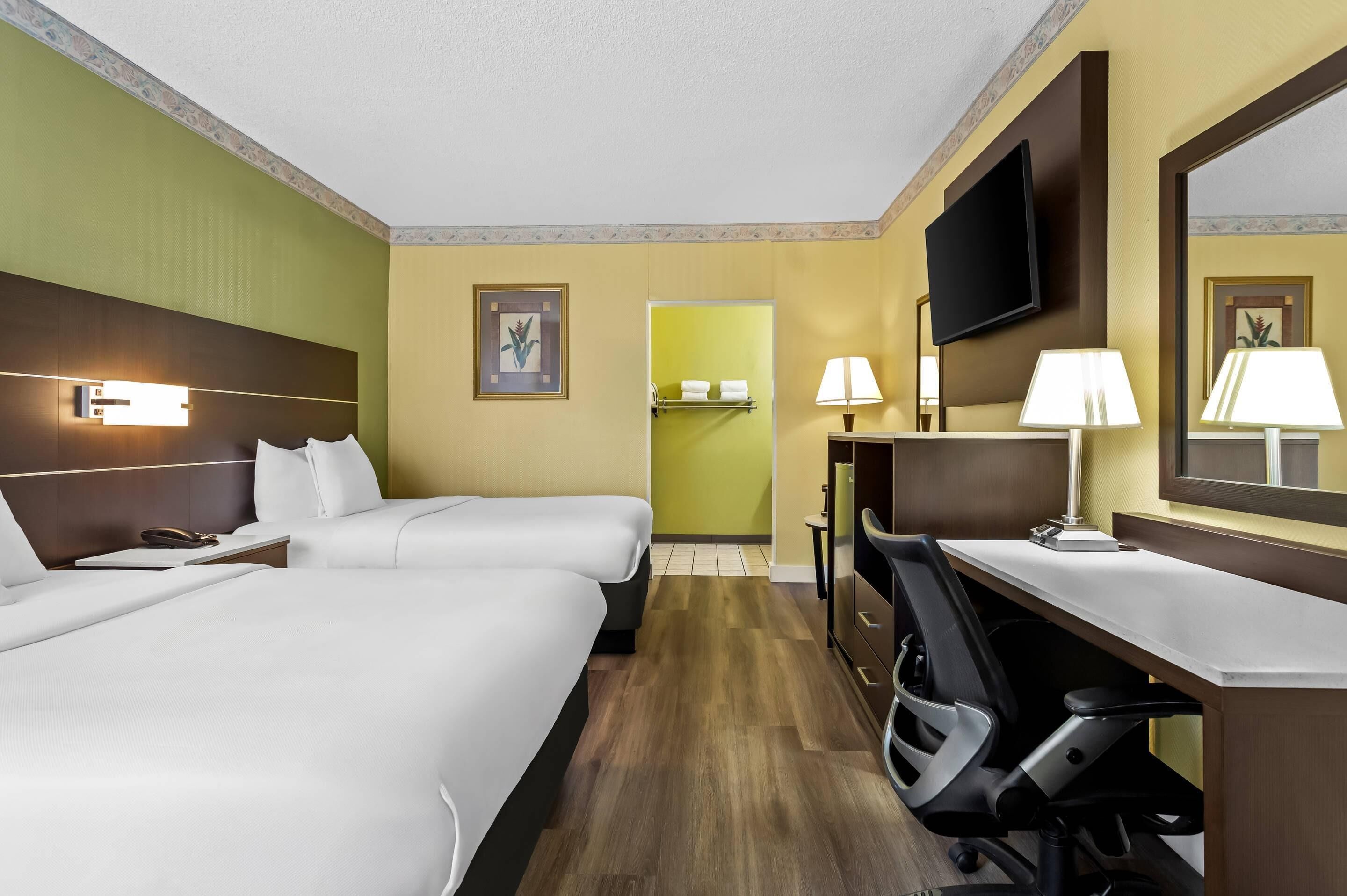 Habitación de hotel con dos camas, un escritorio, una silla, un televisor y la puerta del baño.