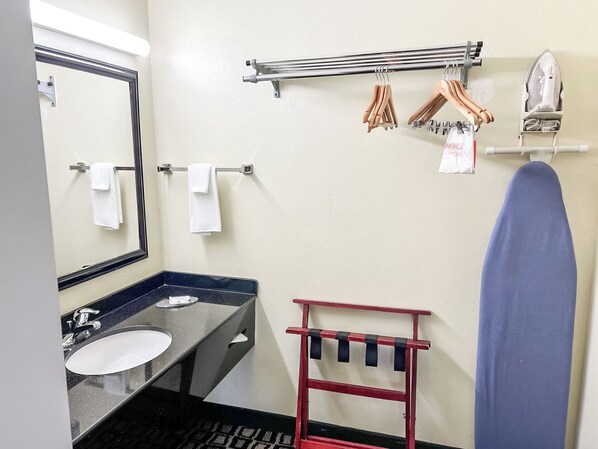 Un baño con lavamanos, espejo, toallero y tabla de planchar.