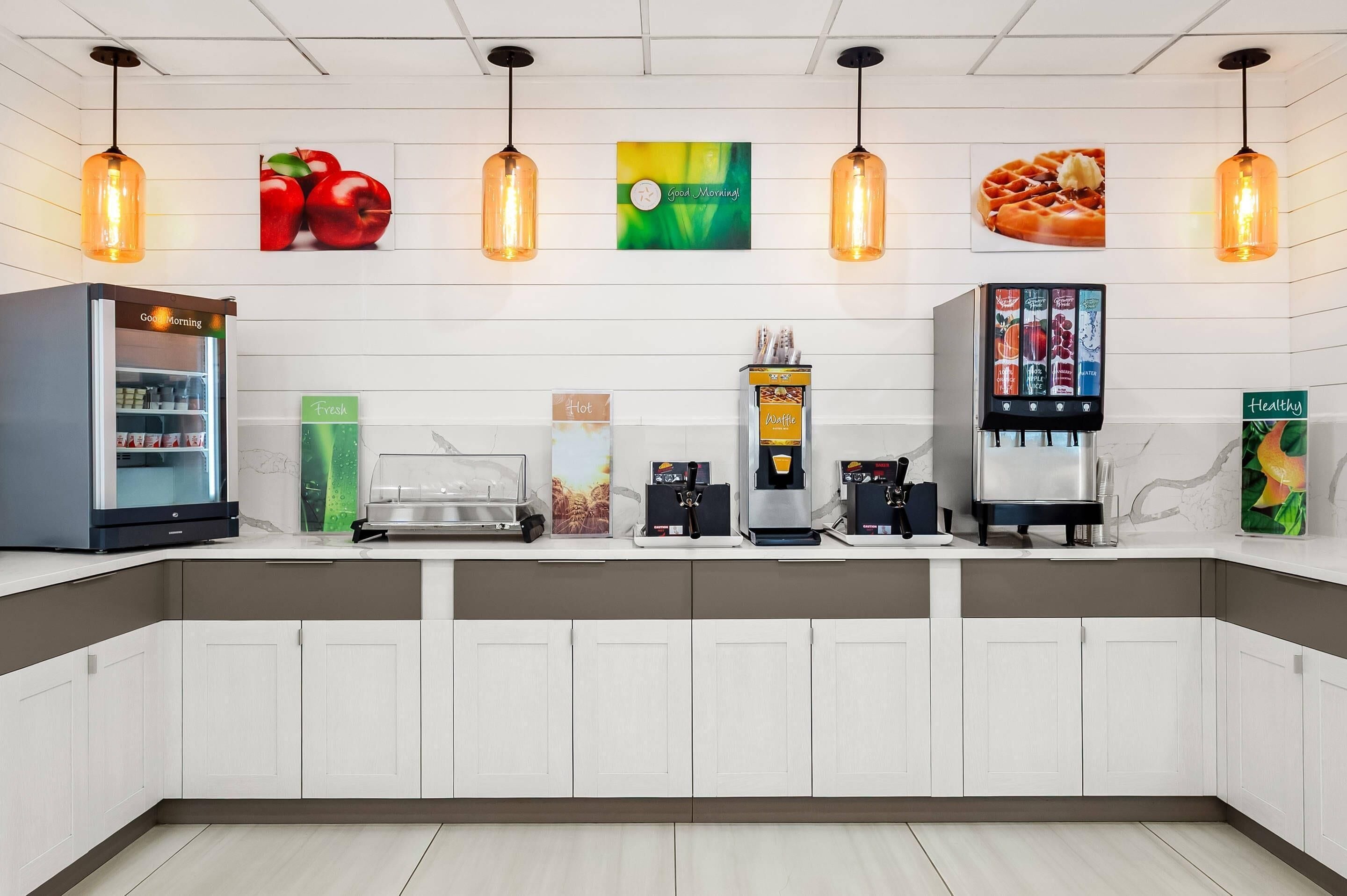 A modern kitchen area with a refrigerator, coffee machines, and a waffle maker.