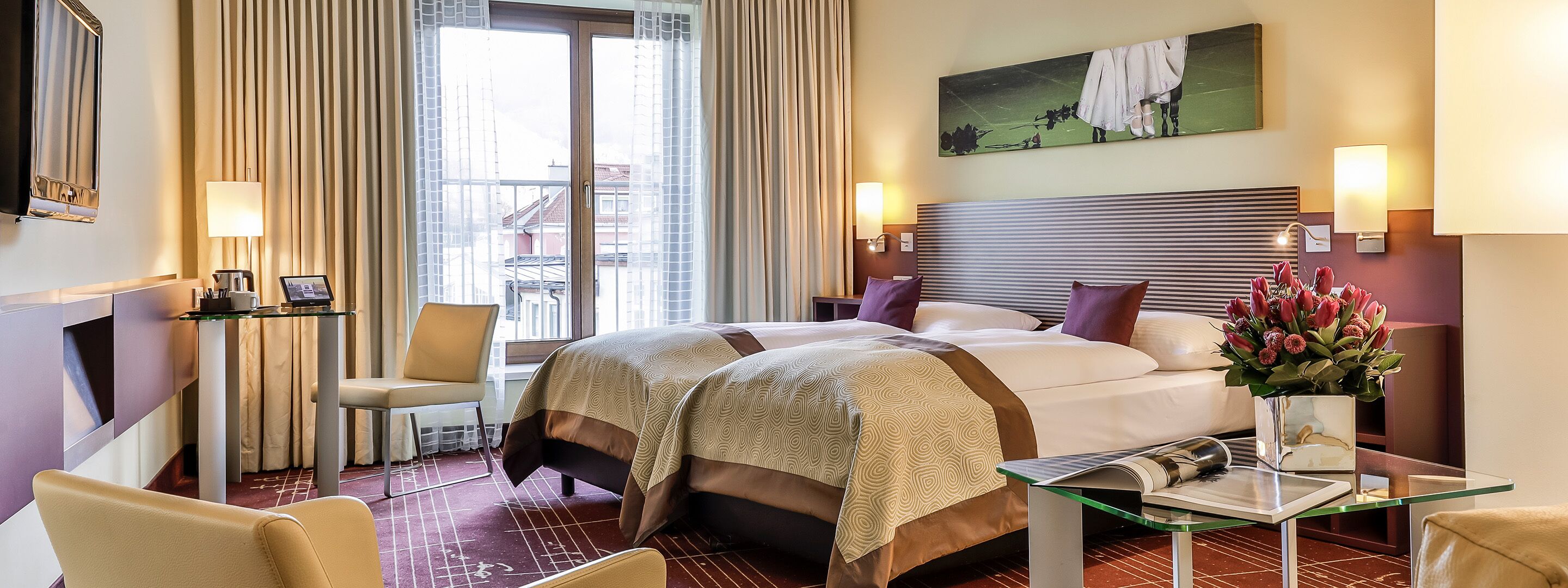 A hotel room with a large bed, two bedside tables, a chair, a desk, and a view of buildings through the window.