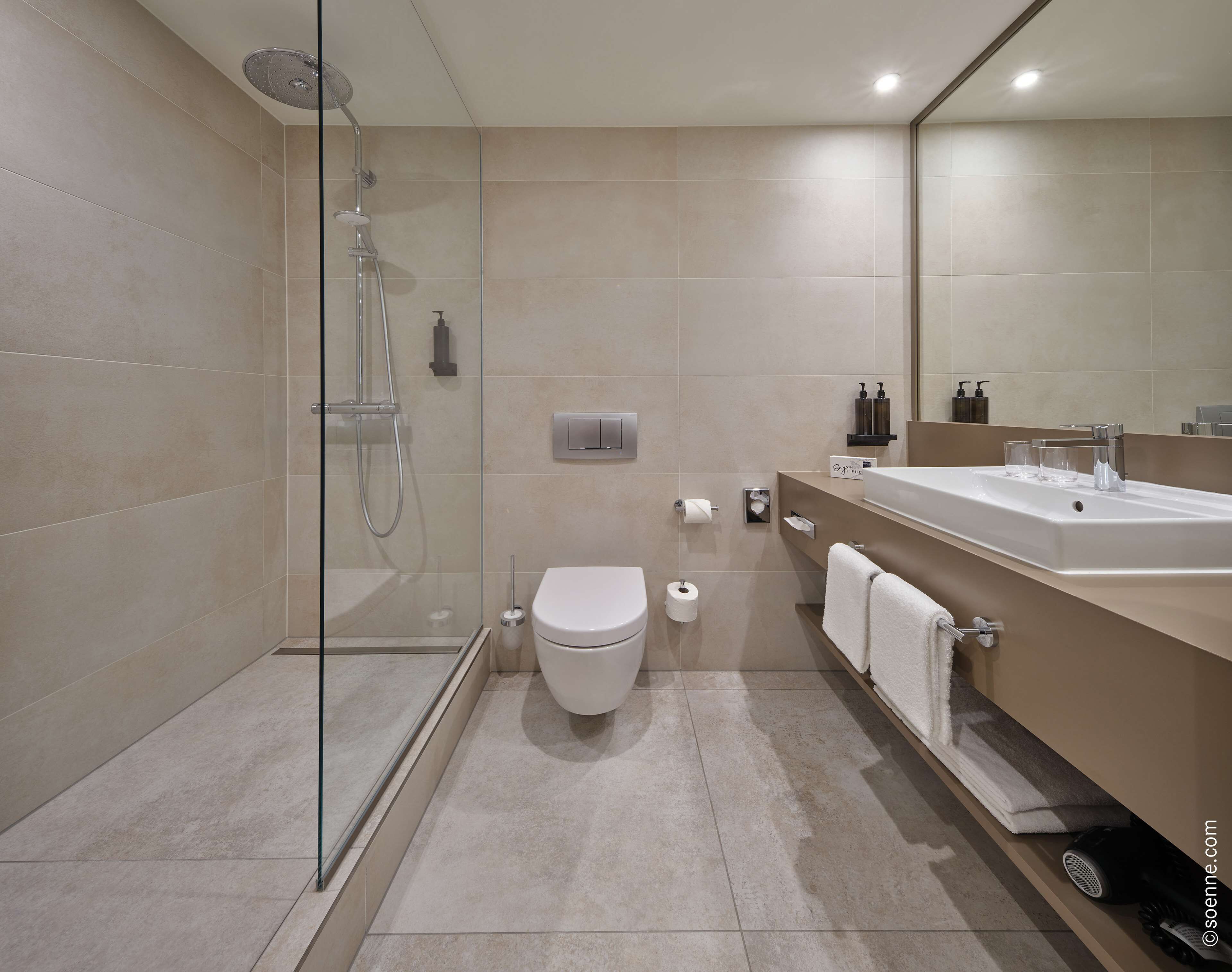 Een moderne badkamer met een douchecabine van glas, een toilet, een wastafel met spiegel en een handdoekrek.