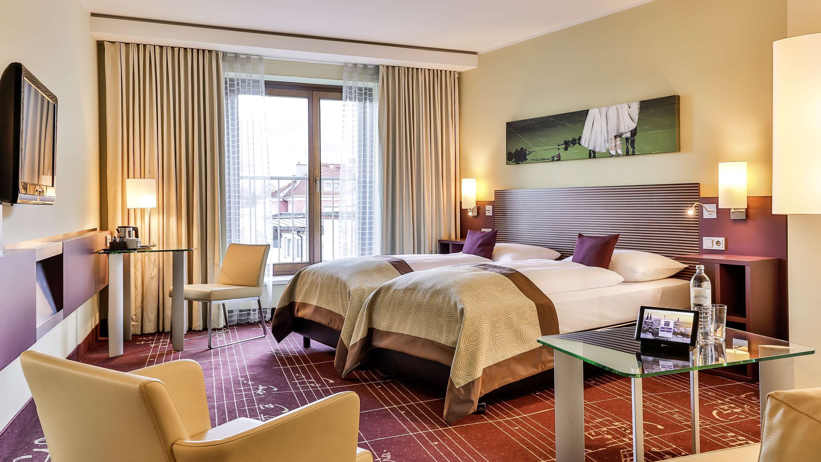A hotel room with a large bed, two bedside tables, a chair, a glass table, and a painting on the wall.