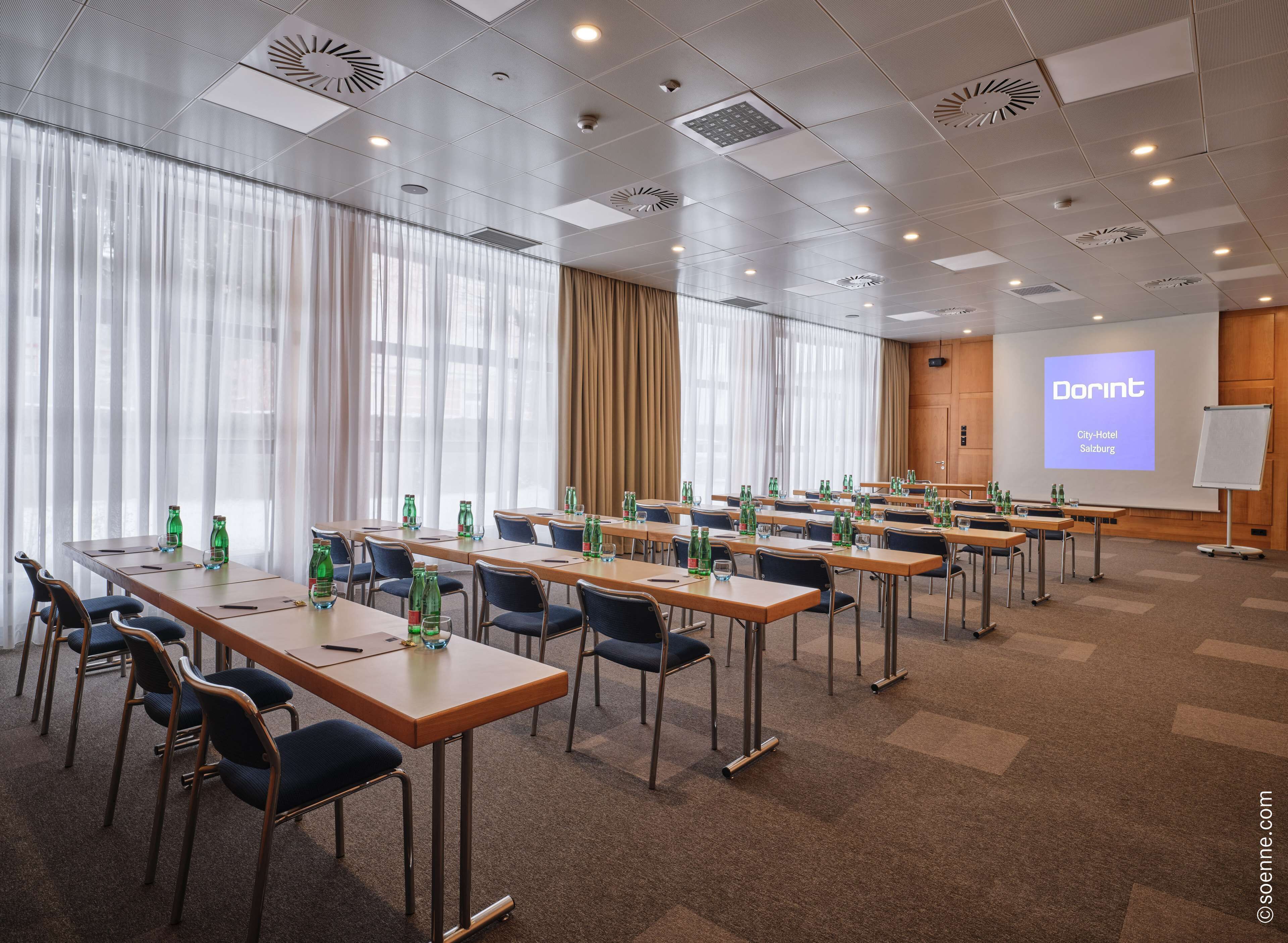A conference room with multiple tables, chairs, and a projector screen displaying 'Dorint City-Hotel Salzburg'.