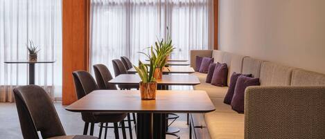 Quarto de hotel moderno com área de refeições, sofá e pequena mesa com plantas.