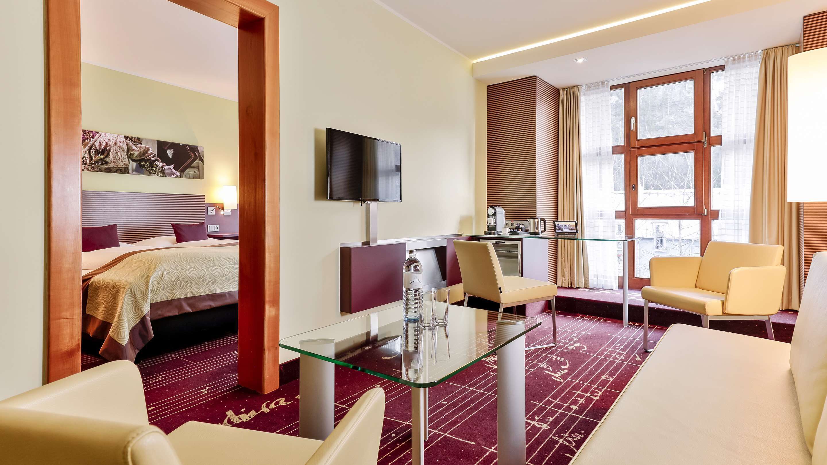 Una habitación de hotel con una cama, televisión, escritorio con silla y zona de estar con dos sillones.