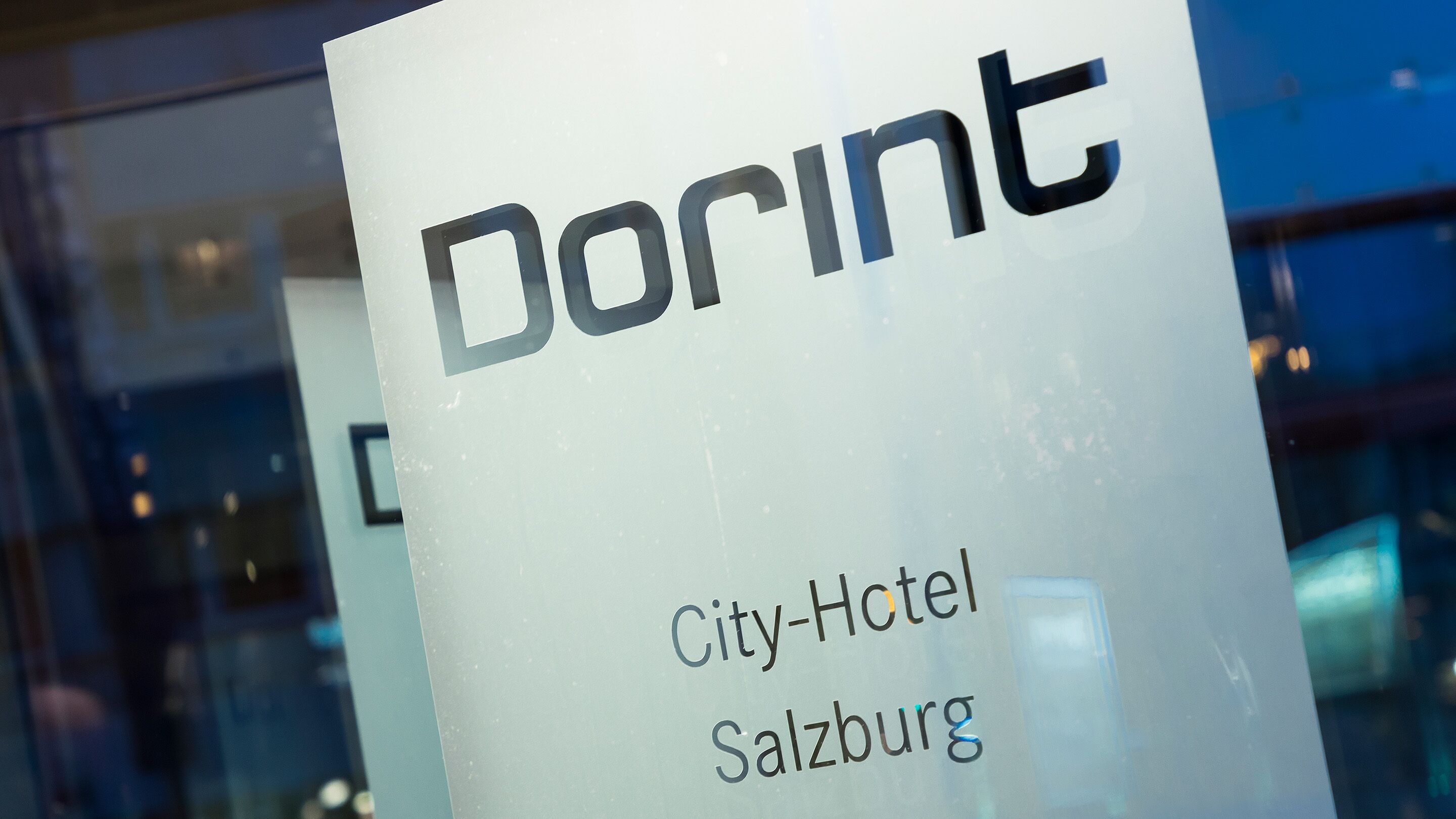 A sign for 'DORINT City-Hotel Salzburg' with a modern glass facade in the background.