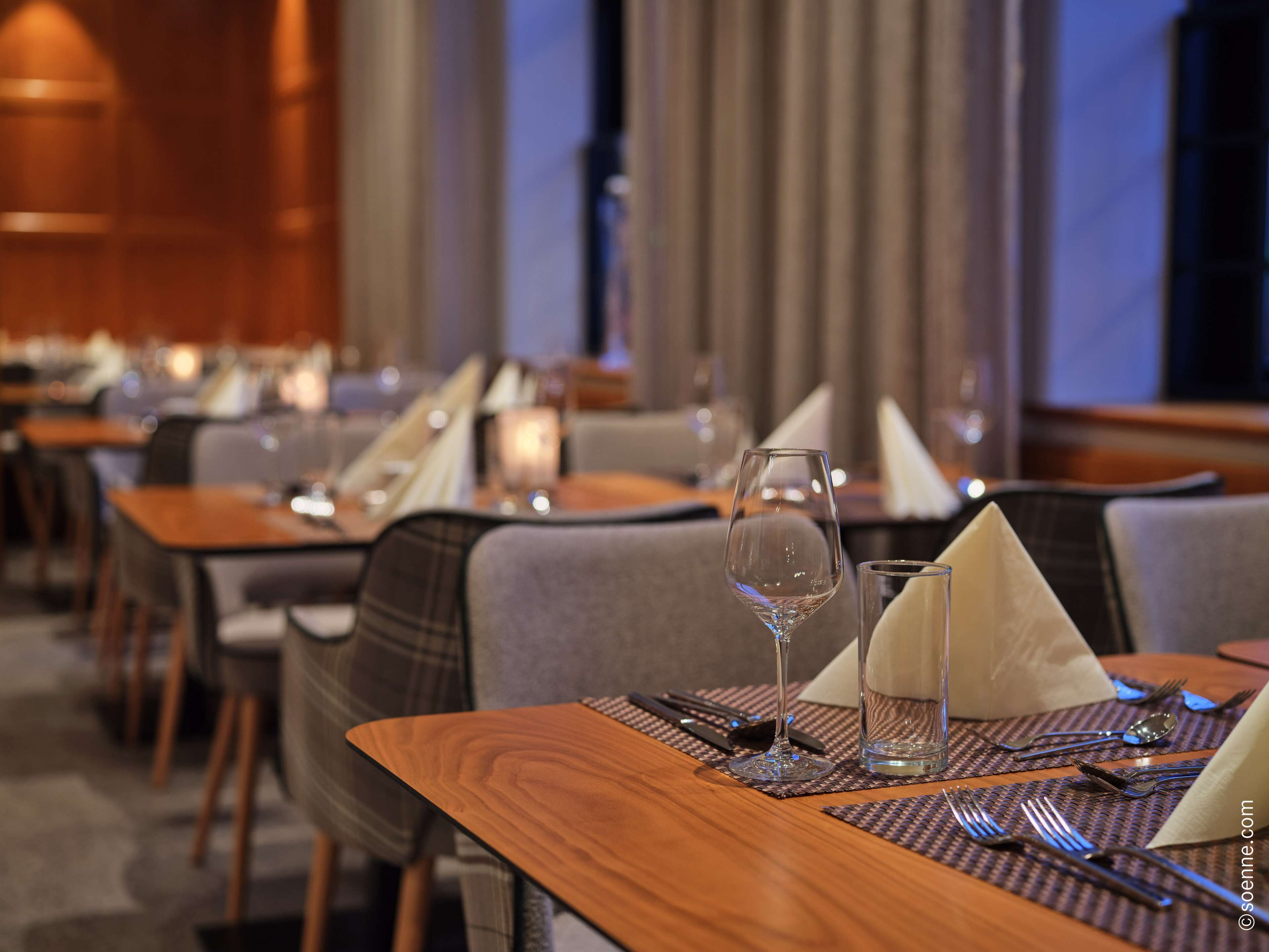 A restaurant setting with tables set for dining, including wine glasses, water glasses, and cutlery.