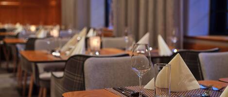 A restaurant setting with tables set for dining, including wine glasses, water glasses, and cutlery.
