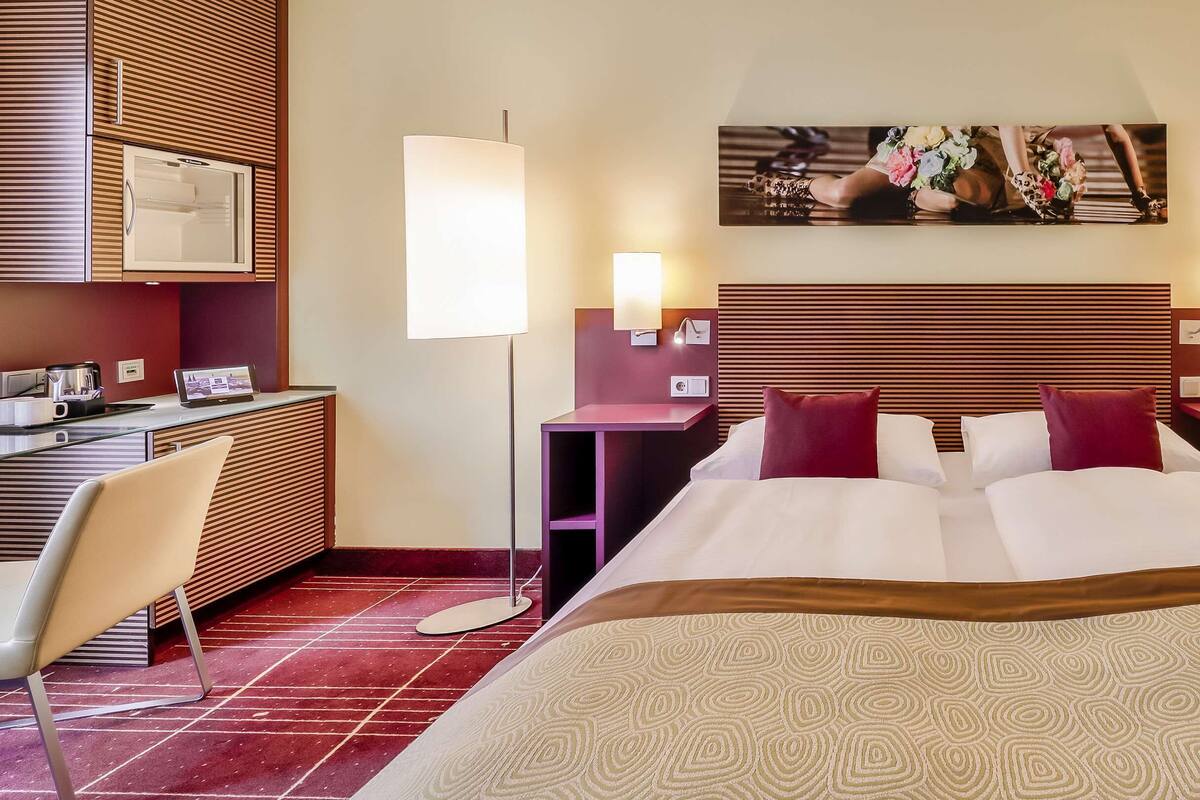 A hotel room with a large bed, a desk, a chair, and a flat-screen TV.