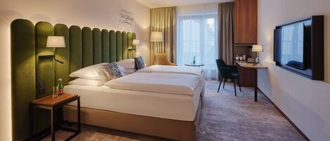 A hotel room with a large bed, a desk, a chair, a TV, and a wall-mounted lamp.