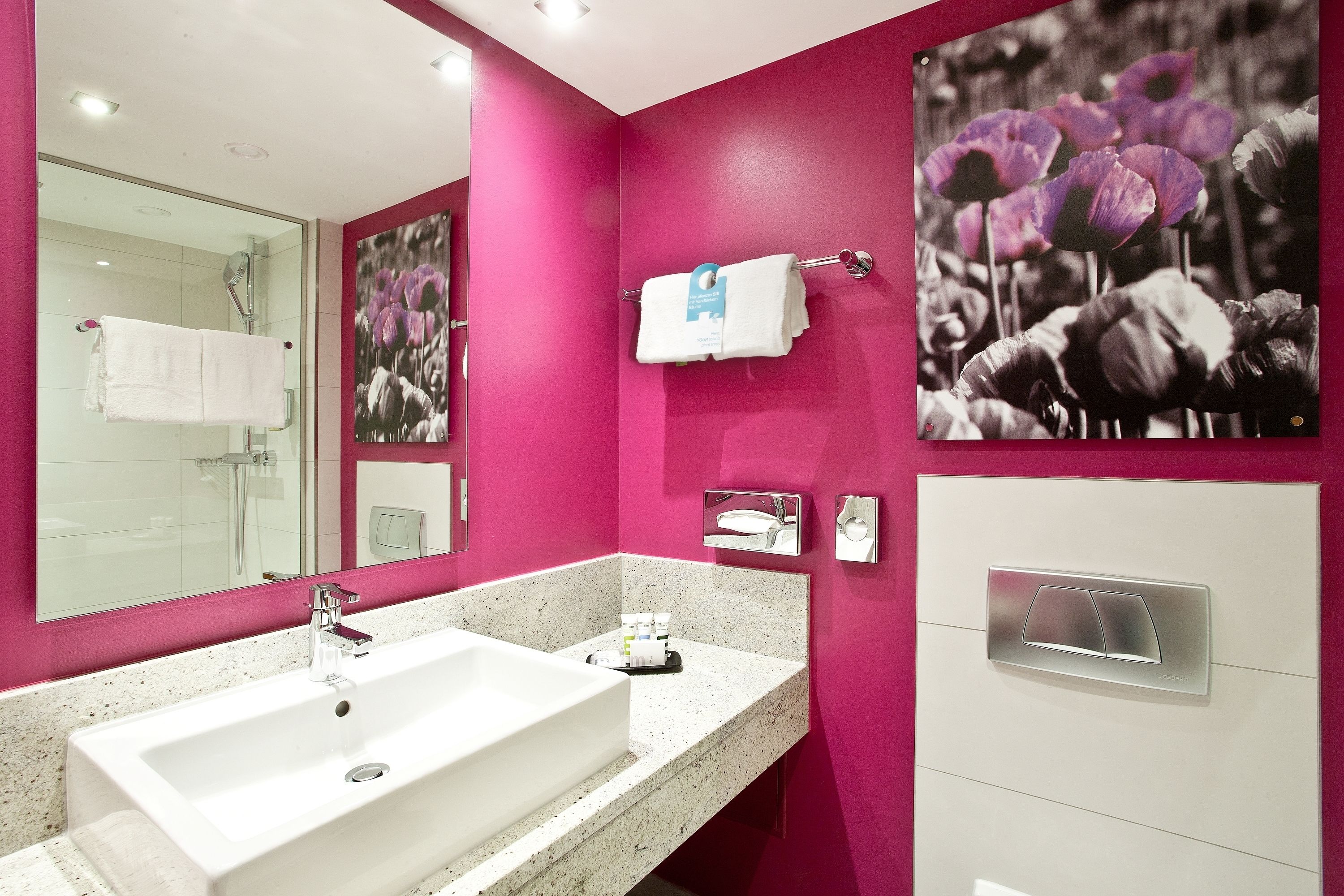 A modern bathroom with a large mirror, a white sink, and a pink accent wall.