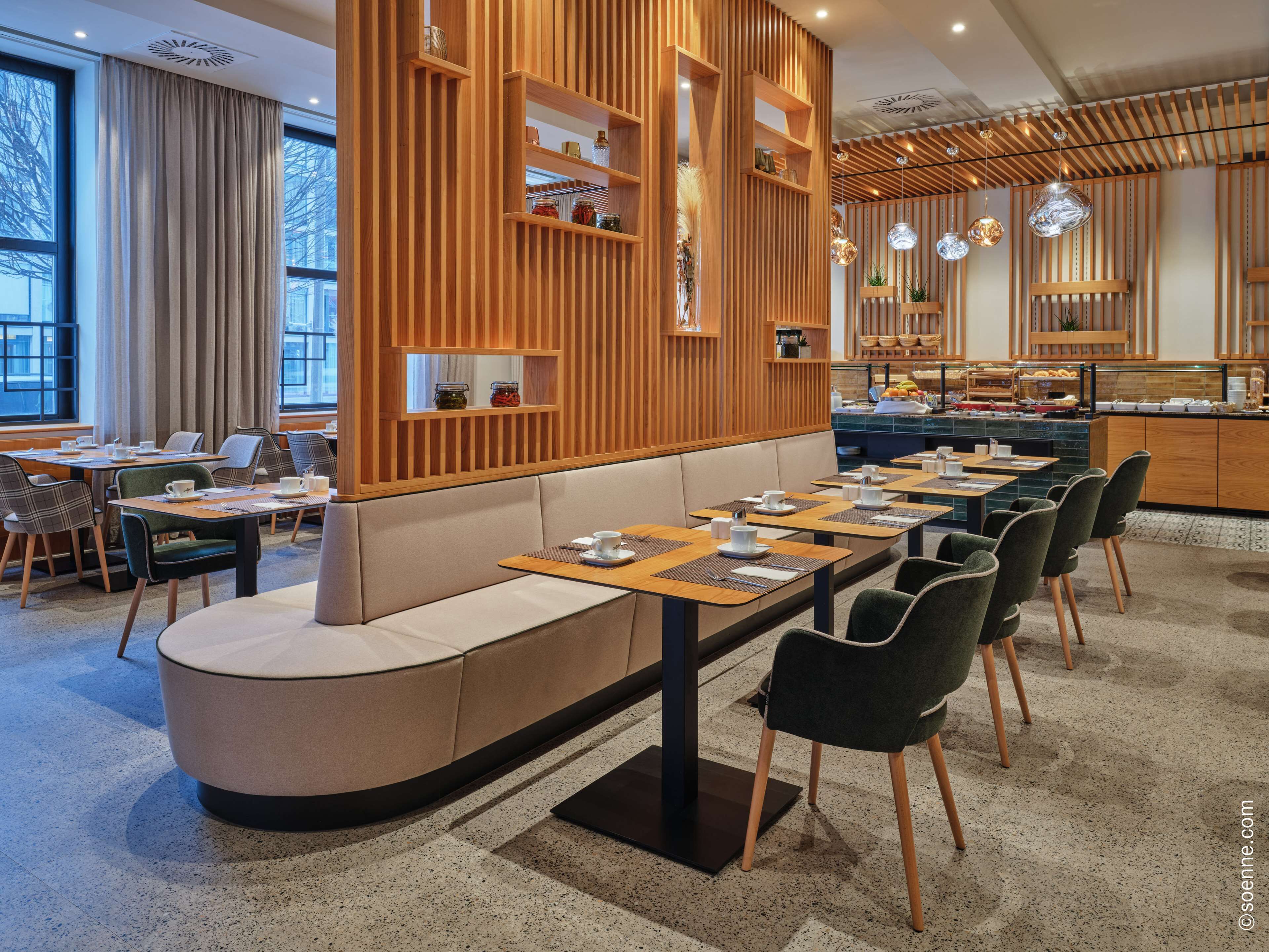 Ein modernes Restaurant mit einem langen Gemeinschaftstisch, bequemen Sitzgelegenheiten und einer Holzwand mit Regalen.
