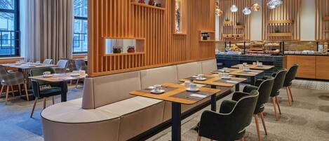 A modern restaurant with a long communal table, cushioned seating, and a wooden partition with shelves.