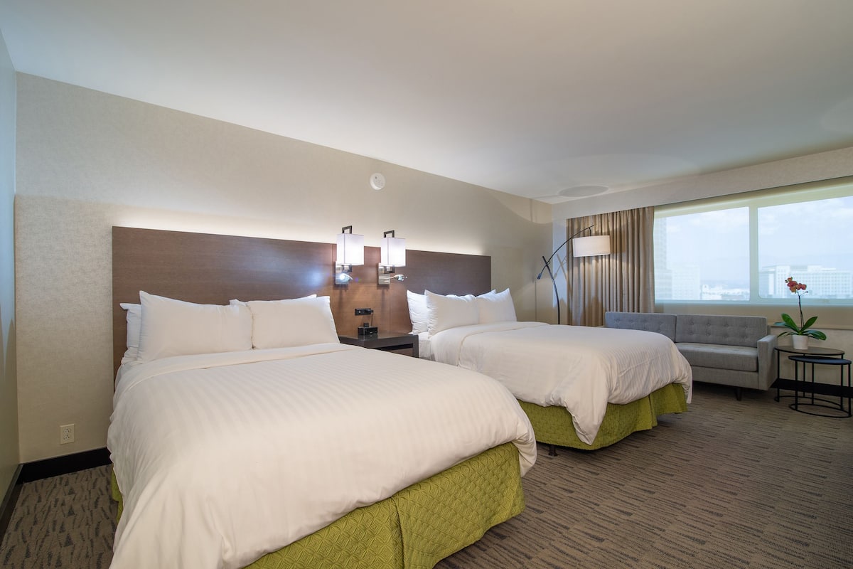 A hotel room with two beds, a sofa, a small table, a lamp, and a window with a view.
