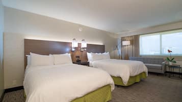 A hotel room with two beds, a sofa, a small table, a lamp, and a window with a view.