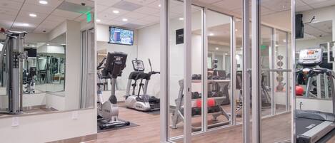 A modern gym with cardio equipment, weight machines, and a mirrored wall.