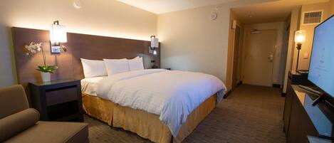 A hotel room with a bed, a nightstand with a lamp, a chair, and a television.