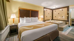 Habitación de hotel con una cama grande, dos lámparas de noche, un baño con bañera y un espejo amplio.
