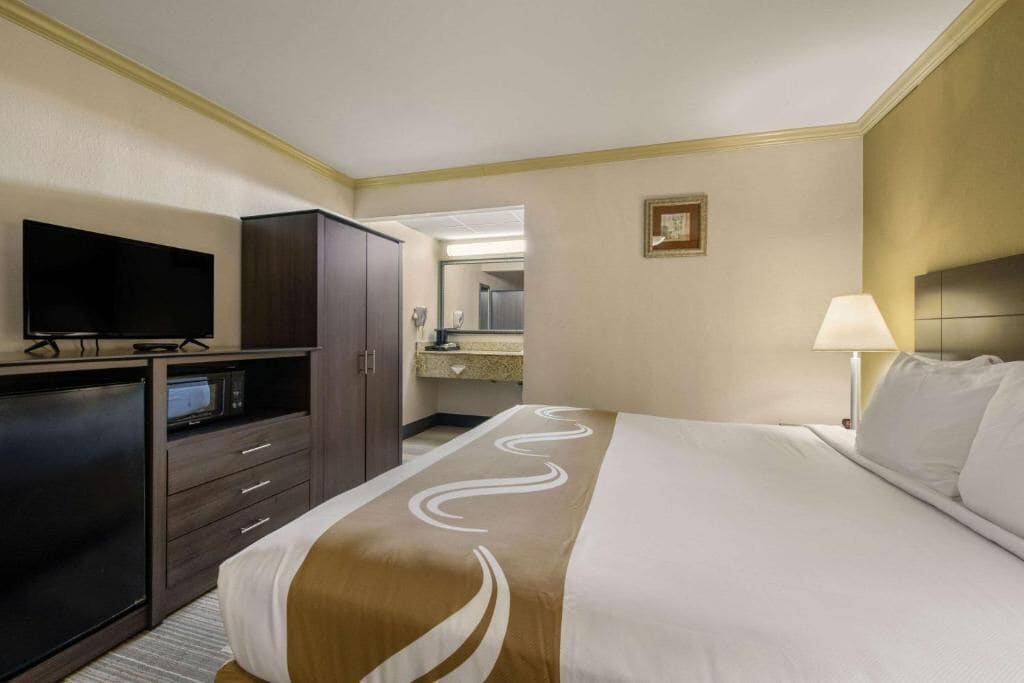 Ett hotellrum med en stor säng, en tv, en garderob och ett badrum som syns genom en öppen dörr.