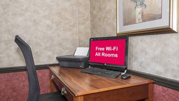 A hotel room with a desk, a laptop, and a sign indicating free Wi-Fi availability.