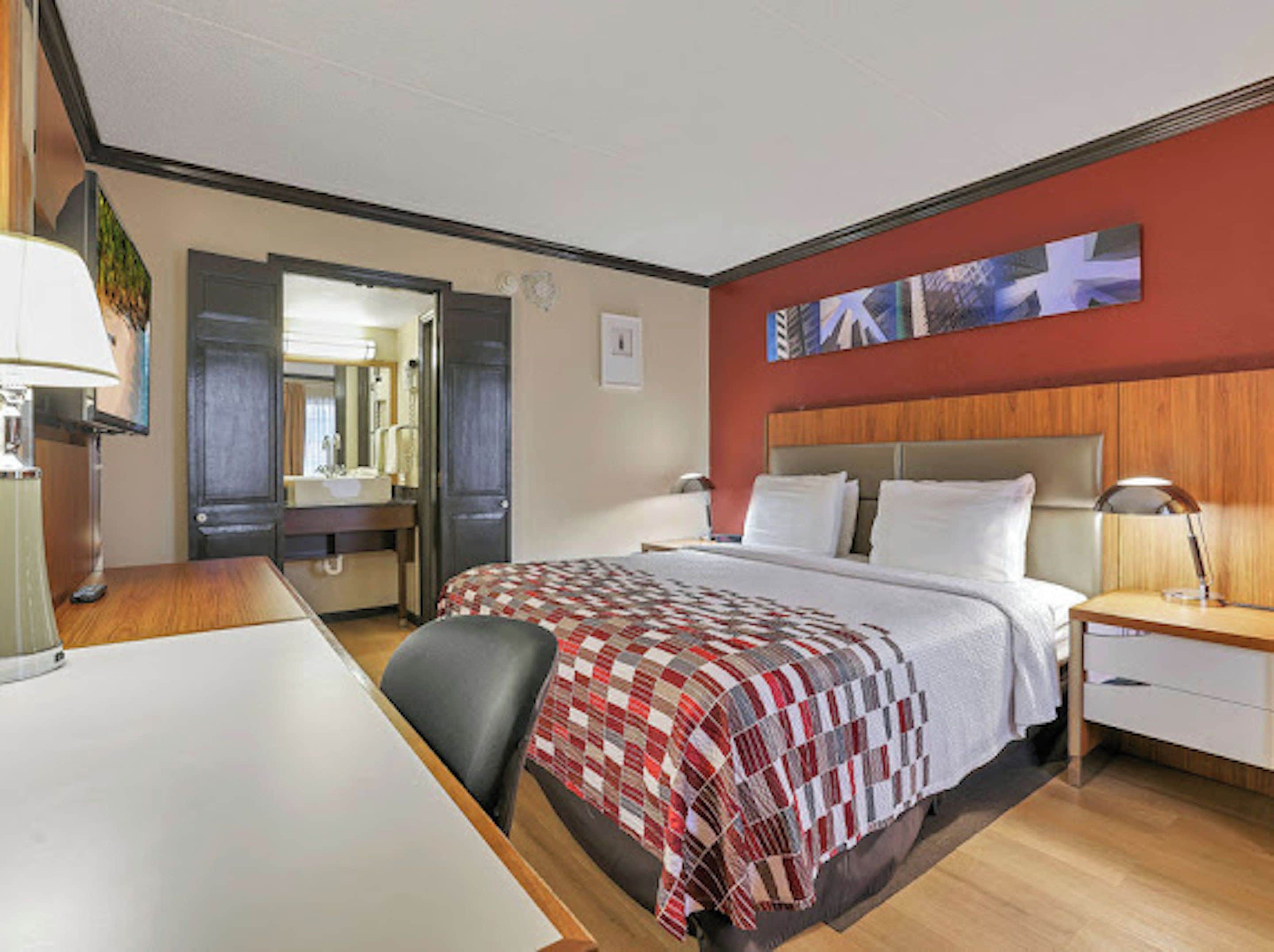 A hotel room with a bed, bedside table, lamp, desk, chair, and a mirror.