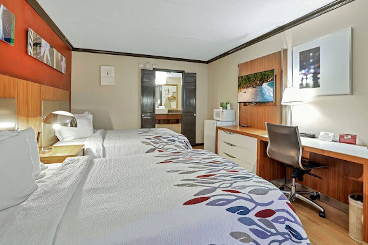 A hotel room with two beds, a desk, a chair, a microwave, and a television.