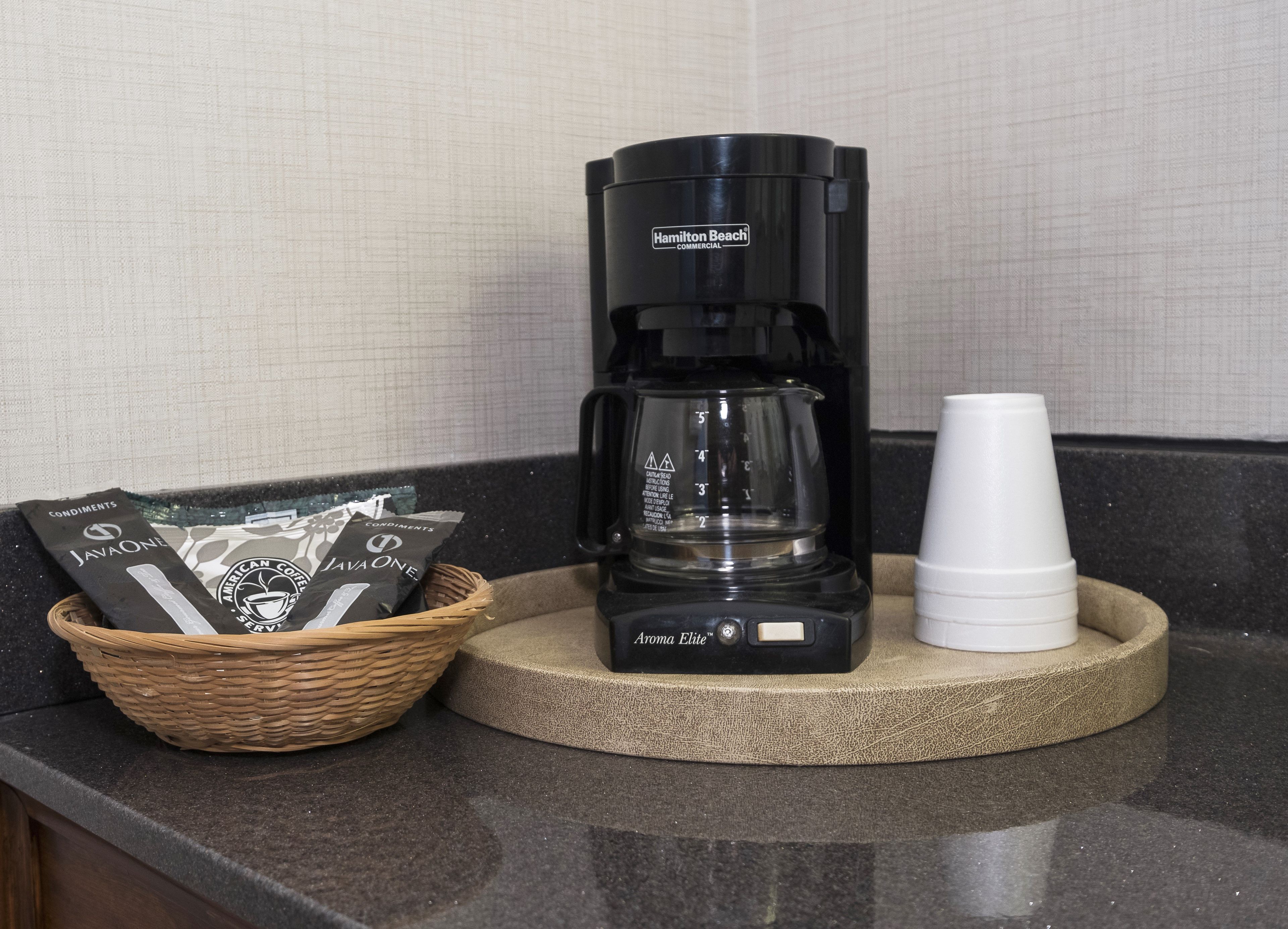 Una cafetera, un cesto de cápsulas de café y una pila de tazas blancas sobre una encimera de cocina.