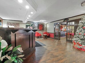 A reception area with a wooden reception desk, red chairs, a Christmas tree, and a wall with a sign. - Red Roof Inn Uhrichsville (Uhrichsville)