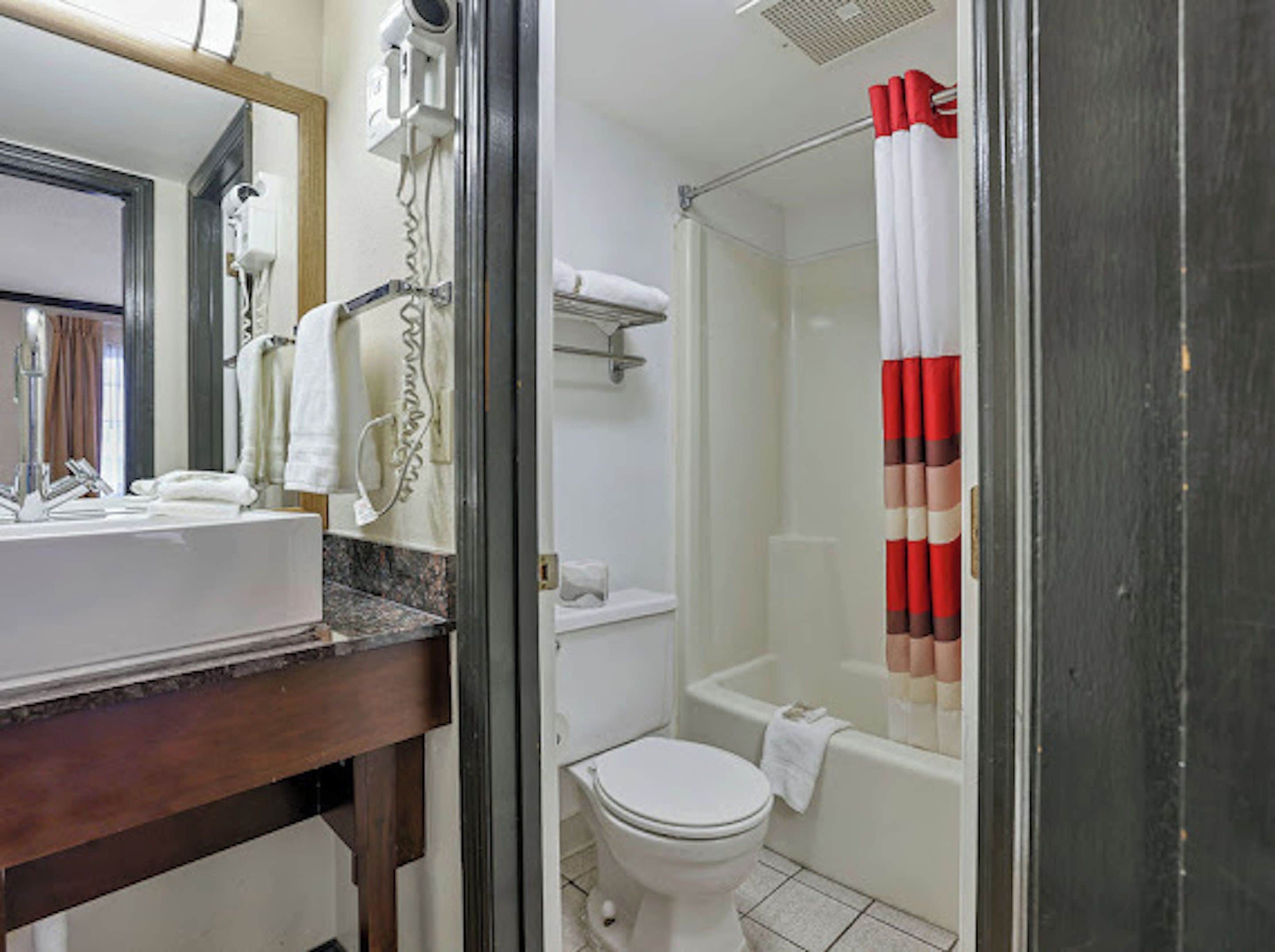 A bathroom with a sink, mirror, towel rack, shower, and toilet.