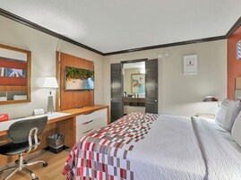 Habitación de hotel con cama, escritorio, silla, televisión y baño visible a través de una puerta abierta.
