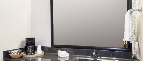 Une salle de bain équipée d’un lavabo, d’une machine à café, d’une serviette et d’un miroir.