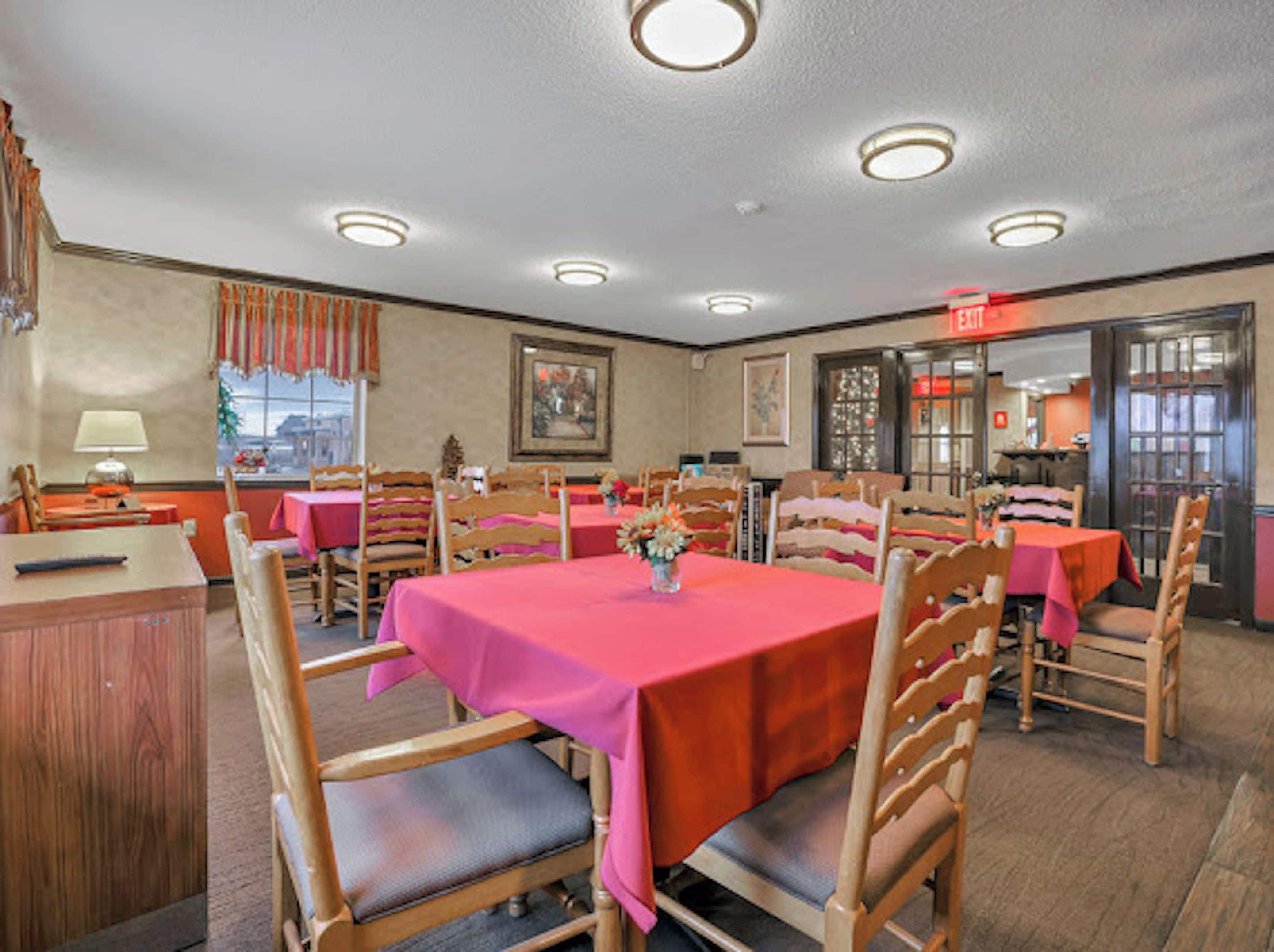 A dining area with multiple tables and chairs, a visible exit sign, and a window with curtains.