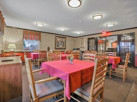 Un comedor con varias mesas y sillas, un letrero de salida visible y una ventana con cortinas.