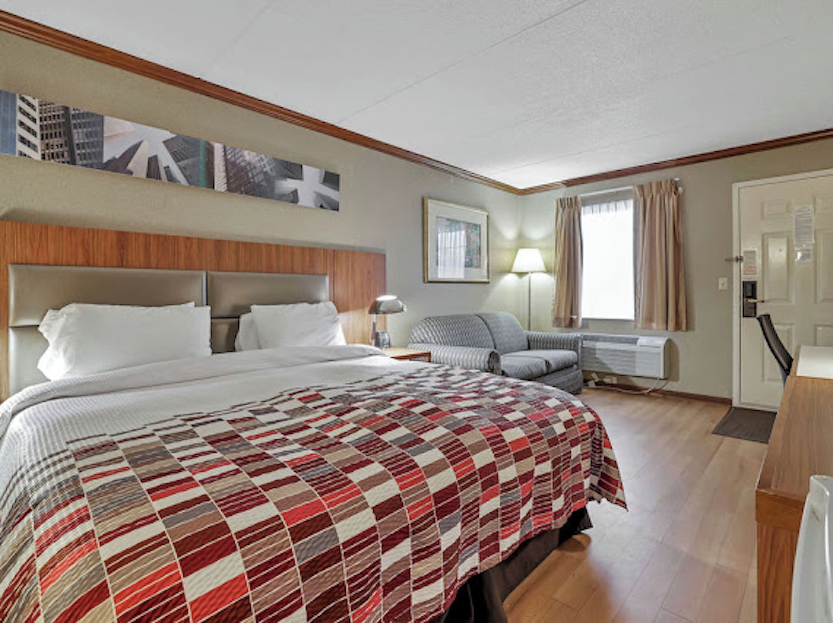 A hotel room with a large bed, a sofa, a desk, and a window with curtains.