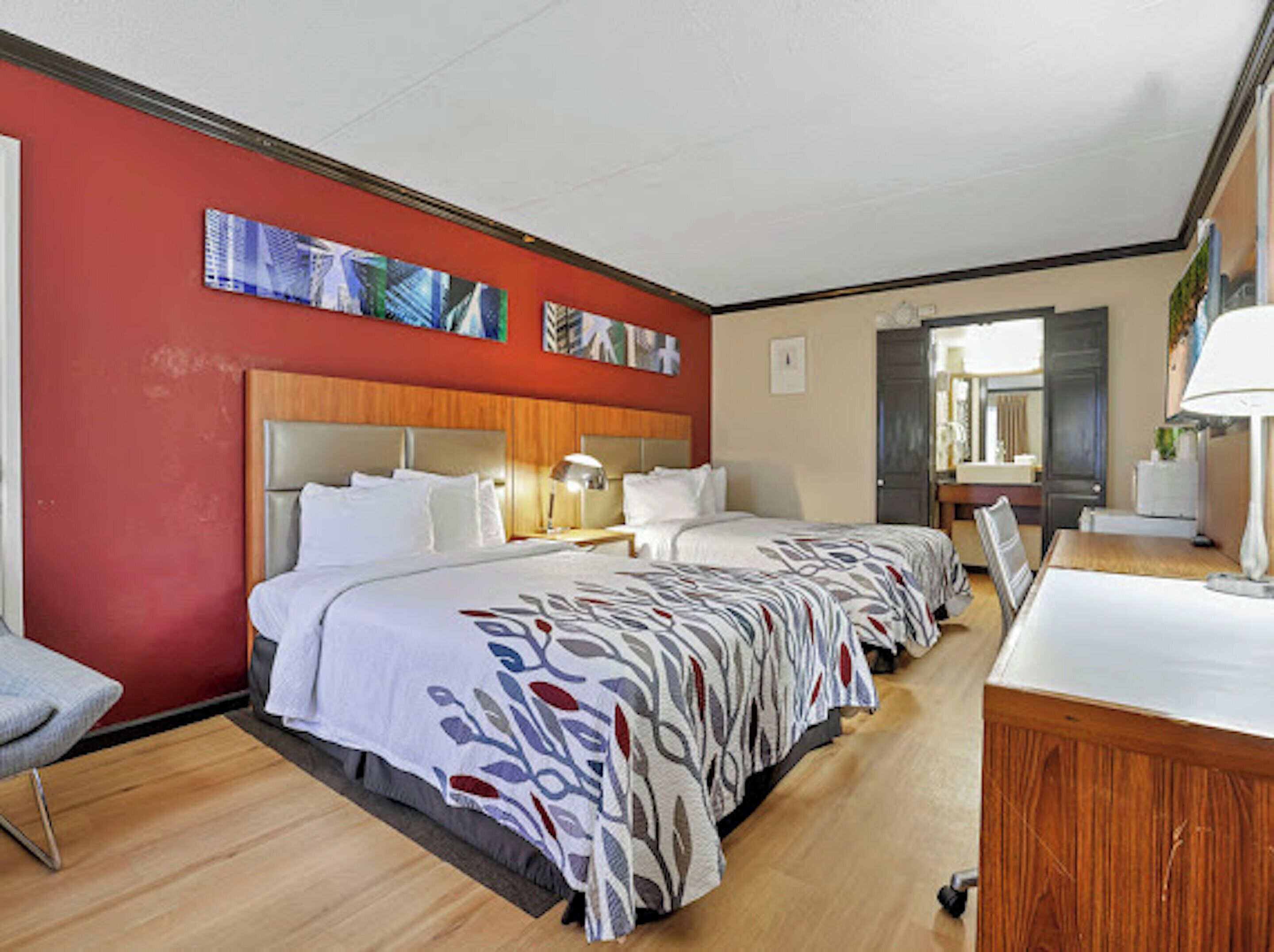 A hotel room with two beds, a wooden headboard, a desk, and a chair.