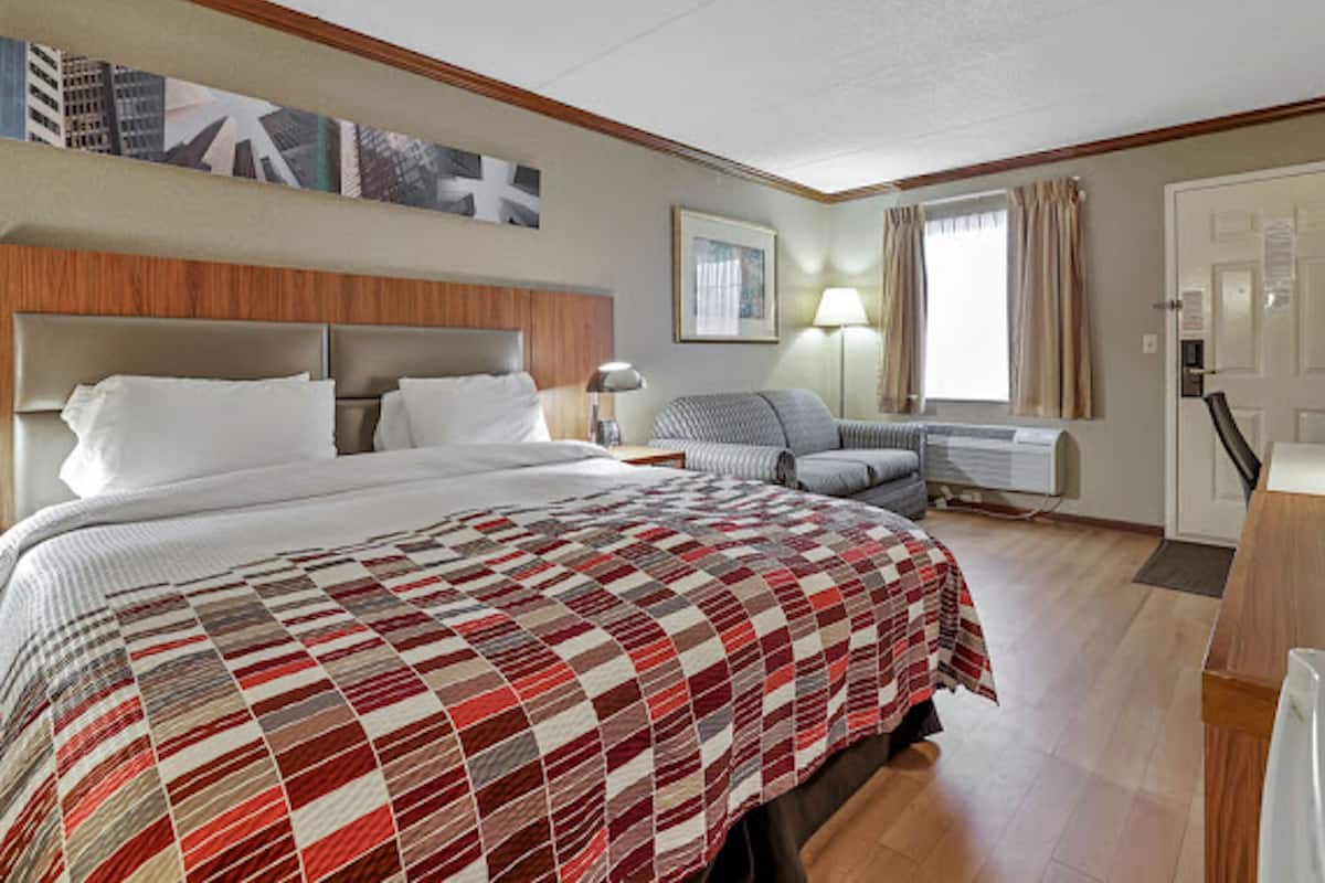 A hotel room with a large bed, a sofa, a desk, and a window with curtains.