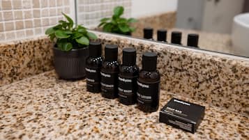 Un meuble-vasque de salle de bain avec un dessus en granit, une plante en pot et plusieurs bouteilles de gel douche et d’après-shampoing de la marque Thankyou.
