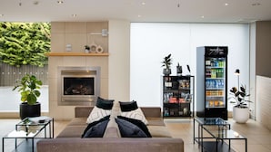 Una sala moderna con chimenea, un sofá con cojines decorativos, una mesa de centro de vidrio, una estantería y una máquina expendedora.