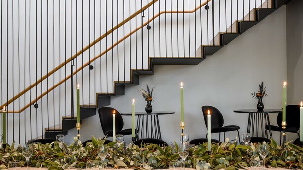 Un comedor con escalera, mesas dispuestas con velas y plantas.