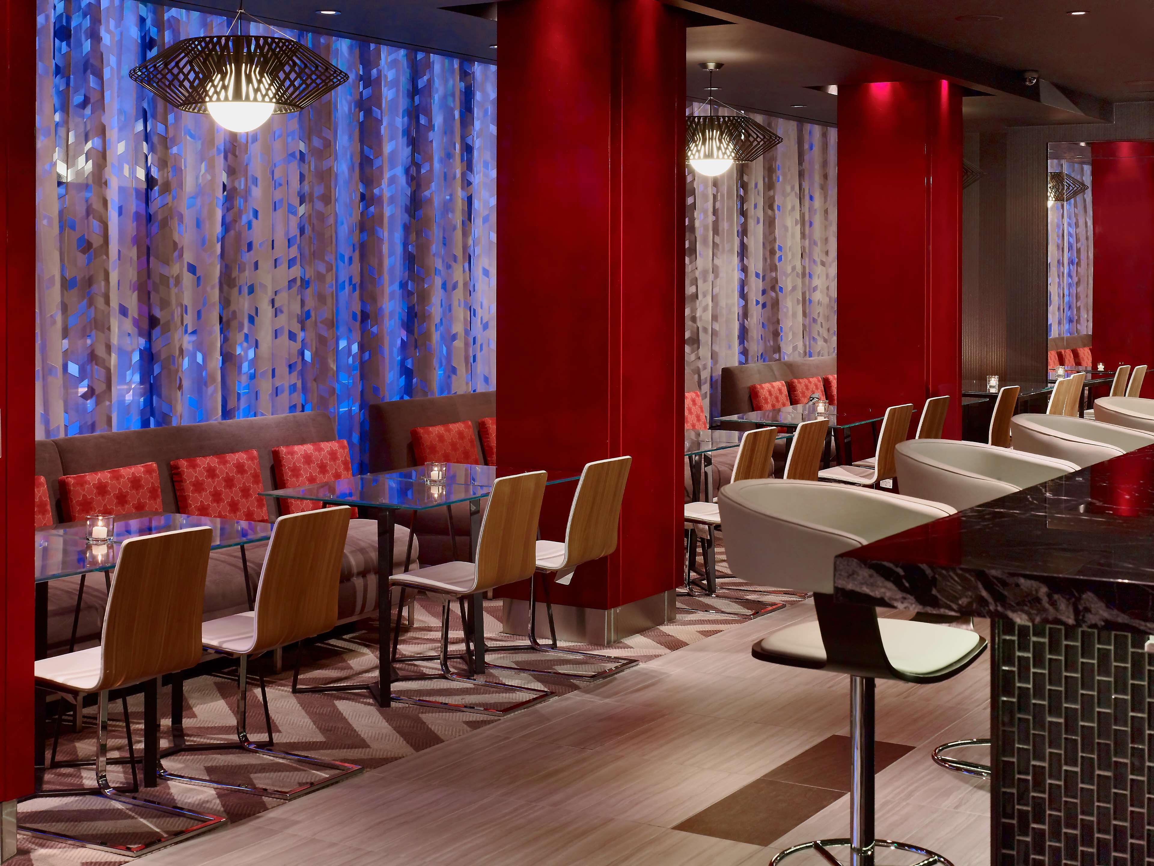 A modern restaurant with glass tables and booths, red accents, and patterned curtains.