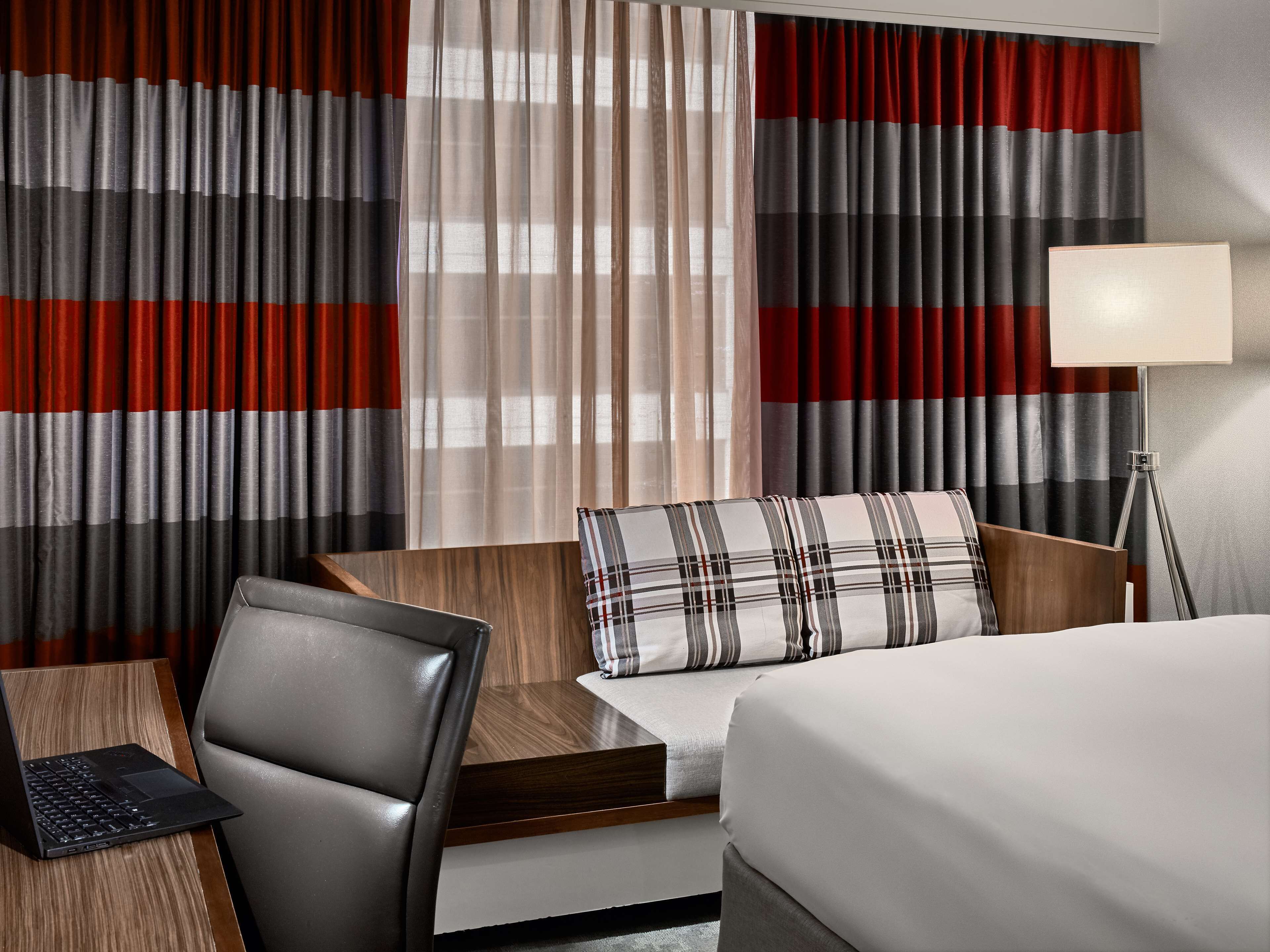 Une chambre d’hôtel avec un lit, un bureau avec un ordinateur portable, une chaise et des rideaux à rayures.