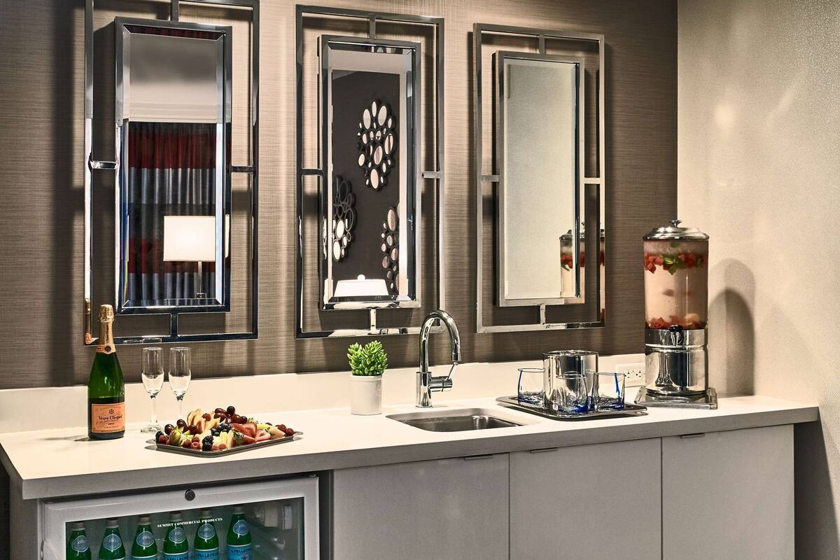 Un bar d’hôtel moderne doté d’un mini-bar, d’un lavabo et de trois miroirs.