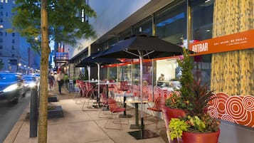 An outdoor seating area with tables and chairs, a sign for Artbar, and a tree in the foreground.