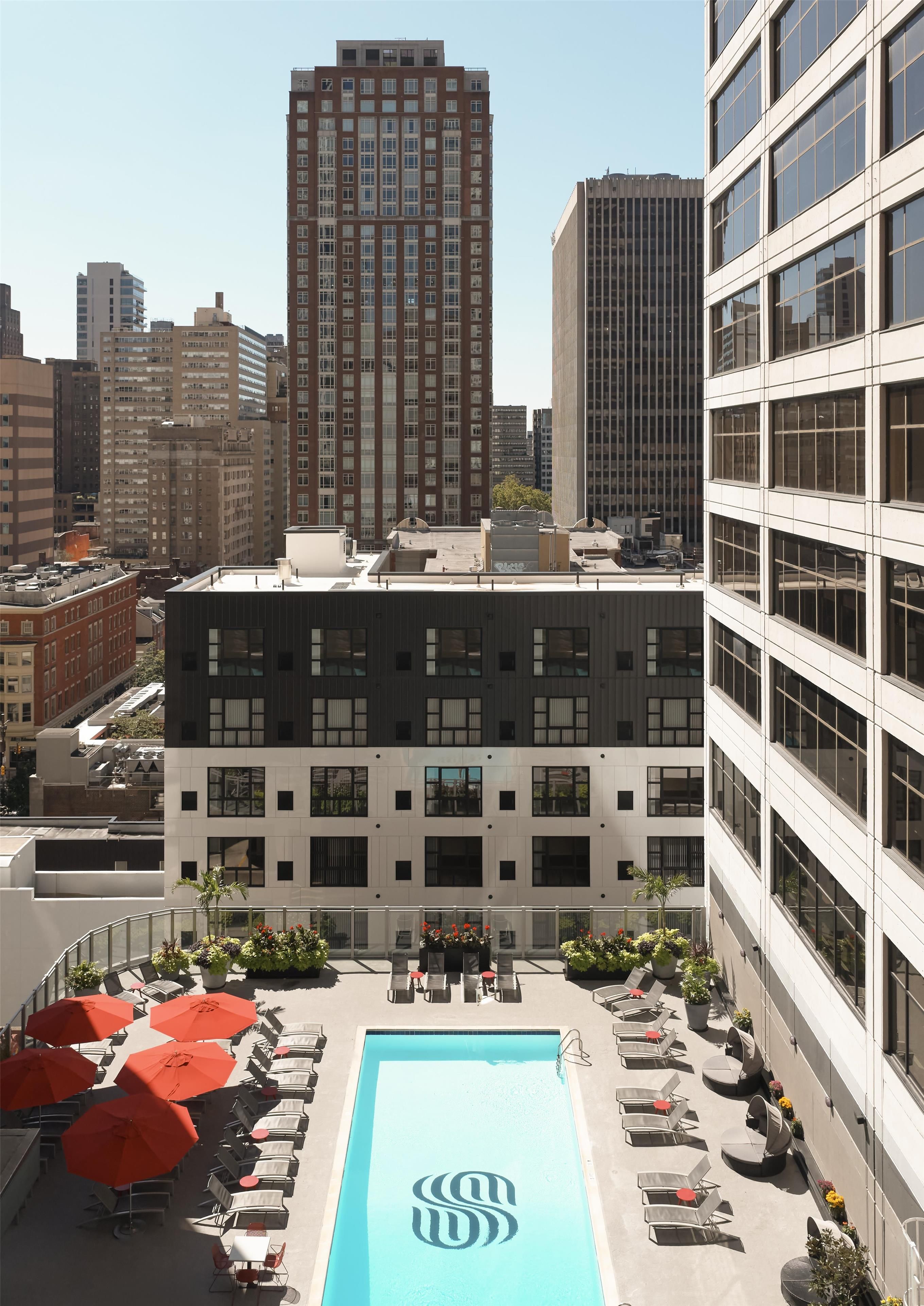 A rooftop pool with lounge chairs and umbrellas, surrounded by high-rise buildings.