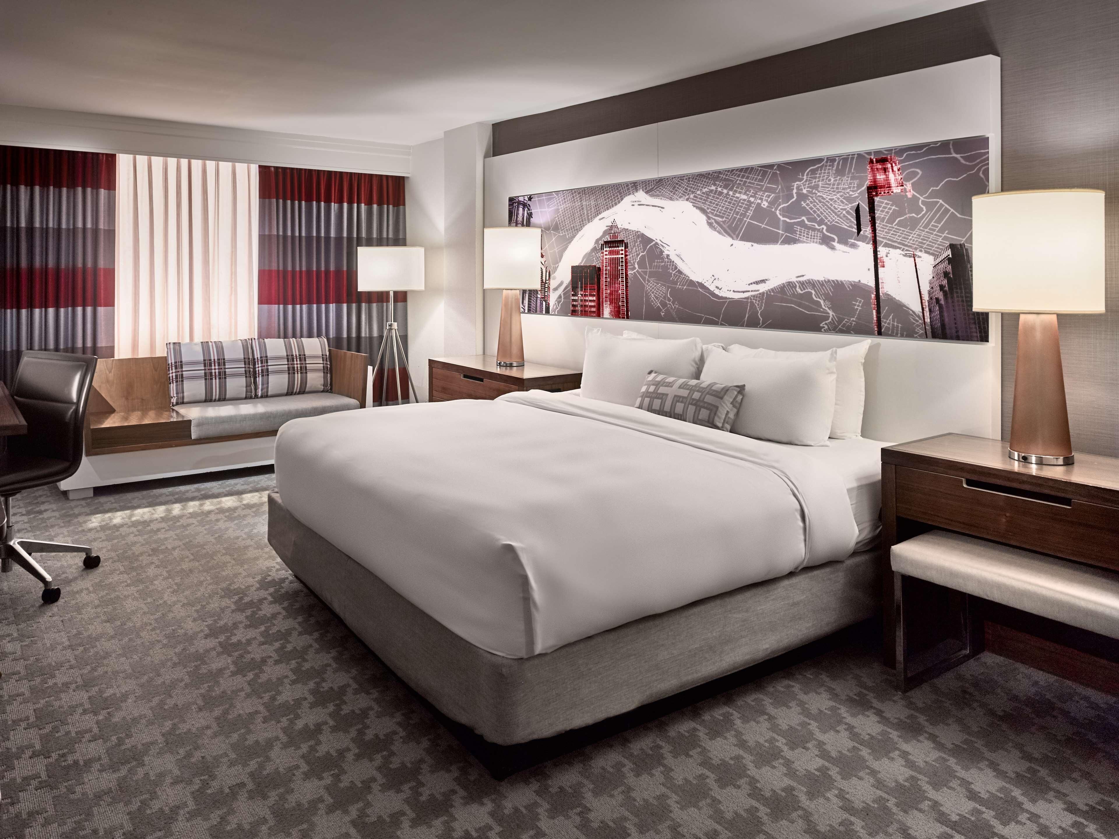 A modern hotel room with a large bed, a sofa, a desk, and a wall-mounted map.