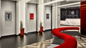 Een moderne lobby met een gebogen bank in rood en grijs, potplanten en een receptiebalie met de naam 'SONESTA'.